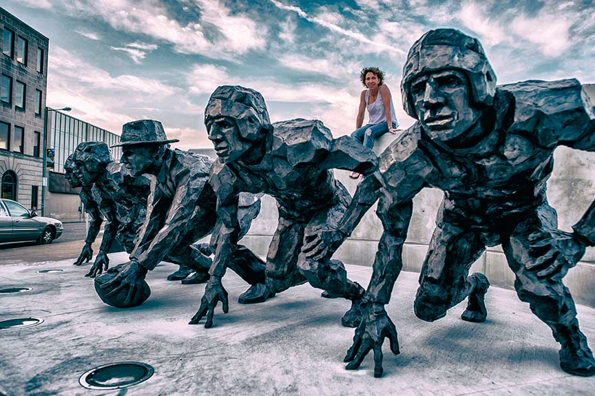 2L-Artist-Gail-Folwell-sitting-behind-her-bronze-sculpture-of-The-NFL-Draft.-photo-Joe-Albert-1